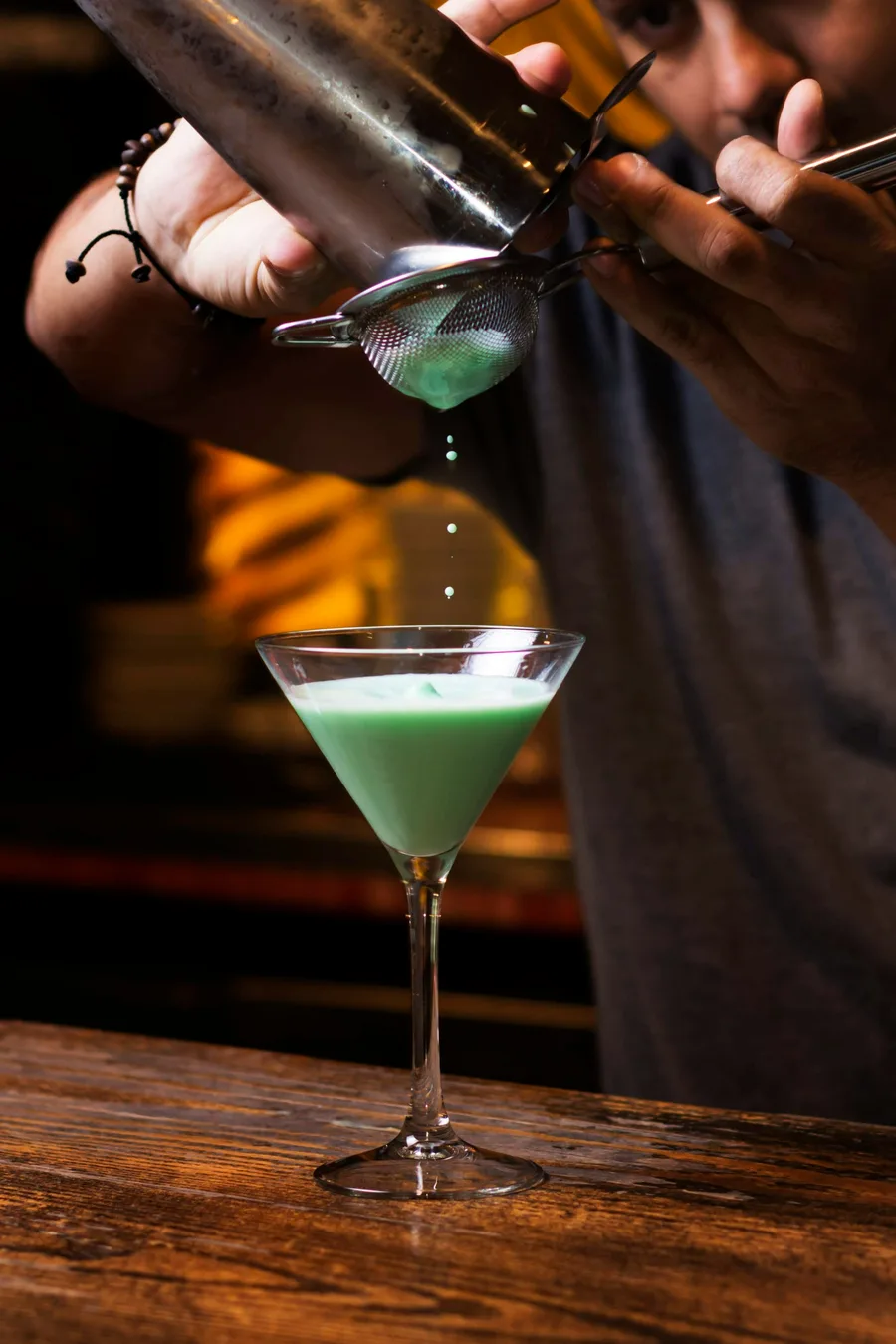 Bartender pouring a green cocktail into a martini glass