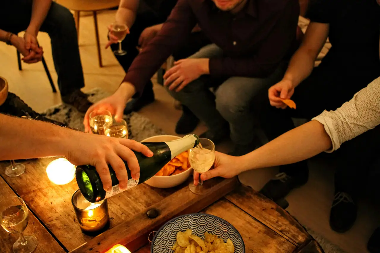 Friends gathered around a coffee table, pouring wine by candlelight